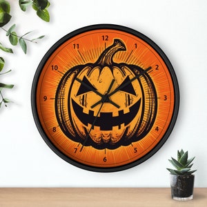 Puede incluir: Un reloj de Halloween negro y naranja con una cara de calabaza. La esfera del reloj tiene agujas negras y números negros.