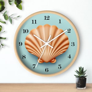 May include: A round wall clock with a light wood frame. The clock face is light blue with a large, detailed seashell in the center. Black numbers mark the hours, and white hands indicate the time. A decorative piece for a coastal theme.