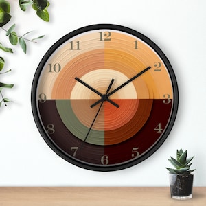 May include: A round wall clock with a black frame and a concentric circle design in shades of brown, beige, and green. The clock face has black Roman numeral hour markers and black hands.