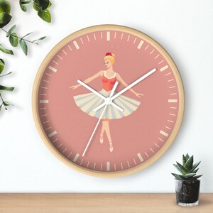 May include: A pink and white clock with a ballerina illustration. The clock has a wooden frame and white hands.