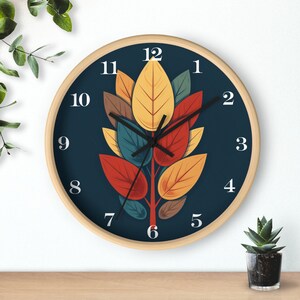 May include: A round wall clock with a dark blue background and a design of colorful leaves in shades of red, yellow, orange, and green. The clock face has white numbers and hands.