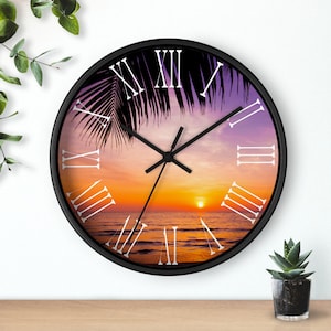 May include: A black framed clock with a sunset beach scene and Roman numeral hour markers. The clock face features a palm tree silhouette and a setting sun over the ocean.