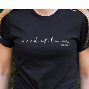 May include: A black t-shirt with the text "maid of honour" in white cursive writing and the word "obviously" in smaller white text below.