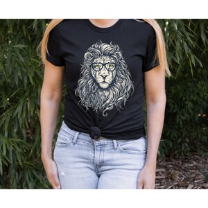 以下が含まれることがあります： 眼鏡をかけたライオンのグラフィックがプリントされた黒いTシャツ。ライオンは白いたてがみと黄色い目をしています。