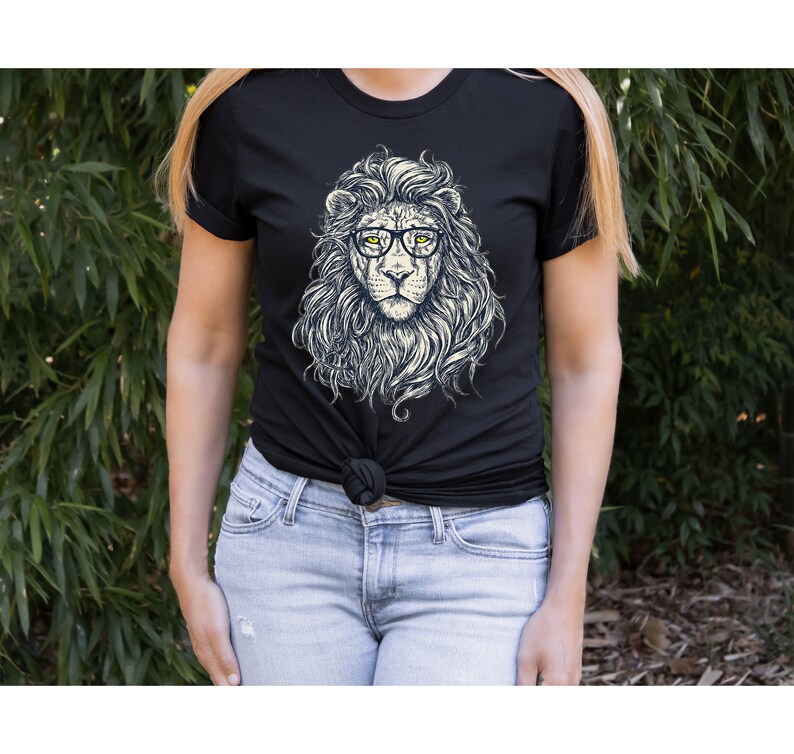 以下が含まれることがあります： 眼鏡をかけたライオンのグラフィックがプリントされた黒いTシャツ。ライオンは白いたてがみと黄色い目をしています。