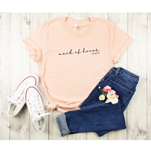 May include: Peach coloured t-shirt with the text "maid of honour" and "obviously" in black script.