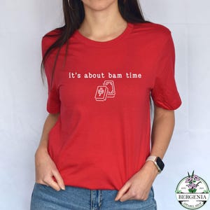 Puede incluir: Camiseta roja con la frase "it's about bam time" en blanco y un gr&aacute;fico de dos fichas de Mahjong. La camiseta tiene cuello redondo y mangas cortas. La tela parece suave y c&oacute;moda.