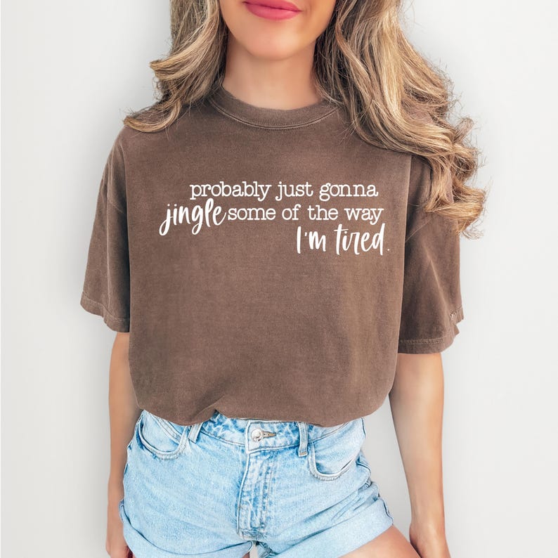 Puede incluir: Camiseta marr&oacute;n con el texto blanco "probably just gonna jingle some of the way I'm tired". La camiseta tiene mangas cortas y un corte relajado. La modelo lleva unos shorts vaqueros azules.