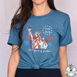 May include: A blue t-shirt featuring a graphic of the Statue of Liberty in red, white, and blue, holding a torch. The shirt includes the text "1776 * 2026" and "250 years of freedom."
