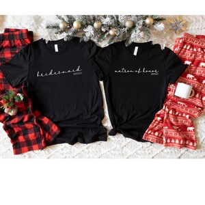 May include: Two black t-shirts with white text. One shirt says "bridesmaid" and the other says "matron of honour".