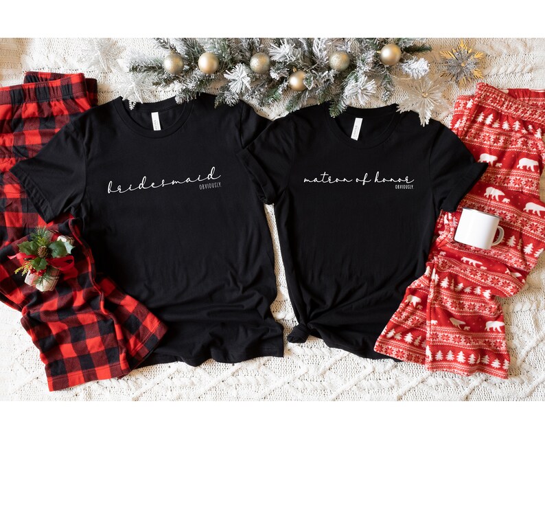 May include: Two black t-shirts with white text. One shirt says "bridesmaid" and the other says "matron of honour".