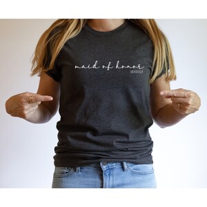 May include: A dark grey t-shirt with the text "maid of honour obviously" in white lettering.