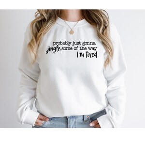 Puede incluir: Sudadera blanca con el texto negro: "probably just gonna jingle some of the way, I'm tired". La sudadera es de cuello redondo y la lleva puesta una persona.