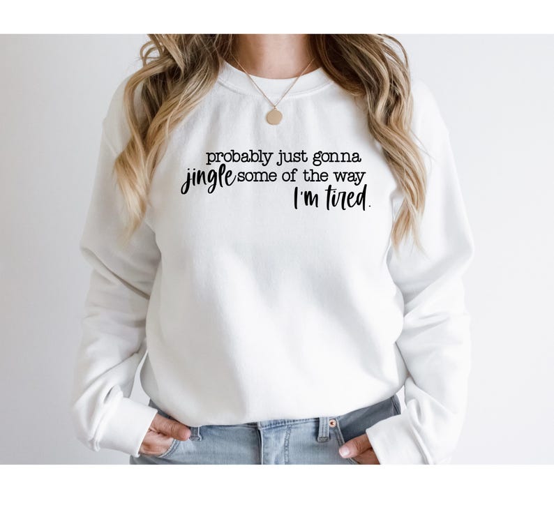 Puede incluir: Sudadera blanca con el texto negro: "probably just gonna jingle some of the way, I'm tired". La sudadera es de cuello redondo y la lleva puesta una persona.