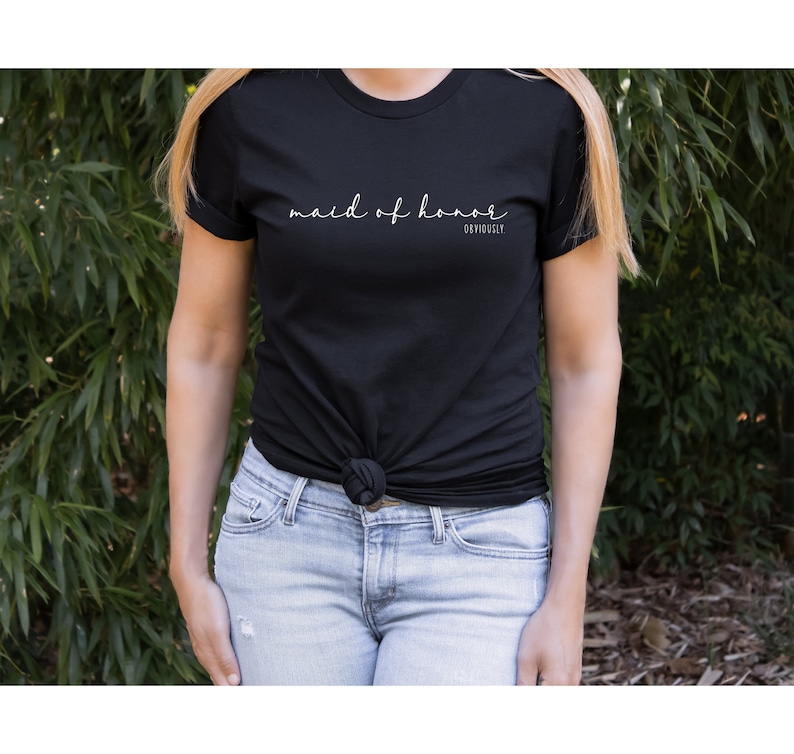 May include: A black t-shirt with the text "maid of honour" in white cursive writing and the word "obviously" in smaller white text below.