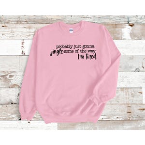 Puede incluir: Sudadera rosa claro con el texto negro: "probably just gonna jingle some of the way, I'm tired". La sudadera tiene cuello redondo y mangas largas.