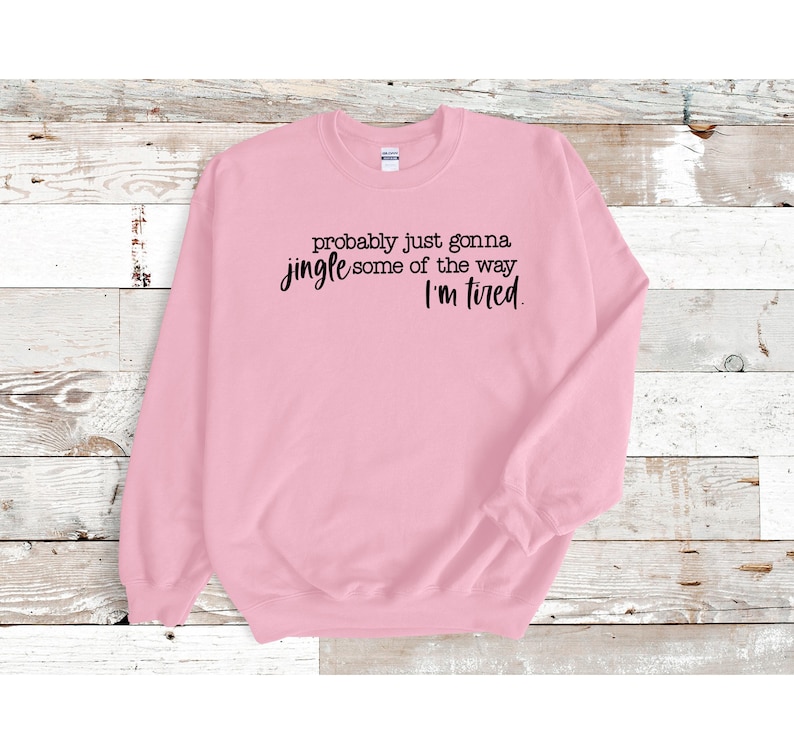 Puede incluir: Sudadera rosa claro con el texto negro: "probably just gonna jingle some of the way, I'm tired". La sudadera tiene cuello redondo y mangas largas.