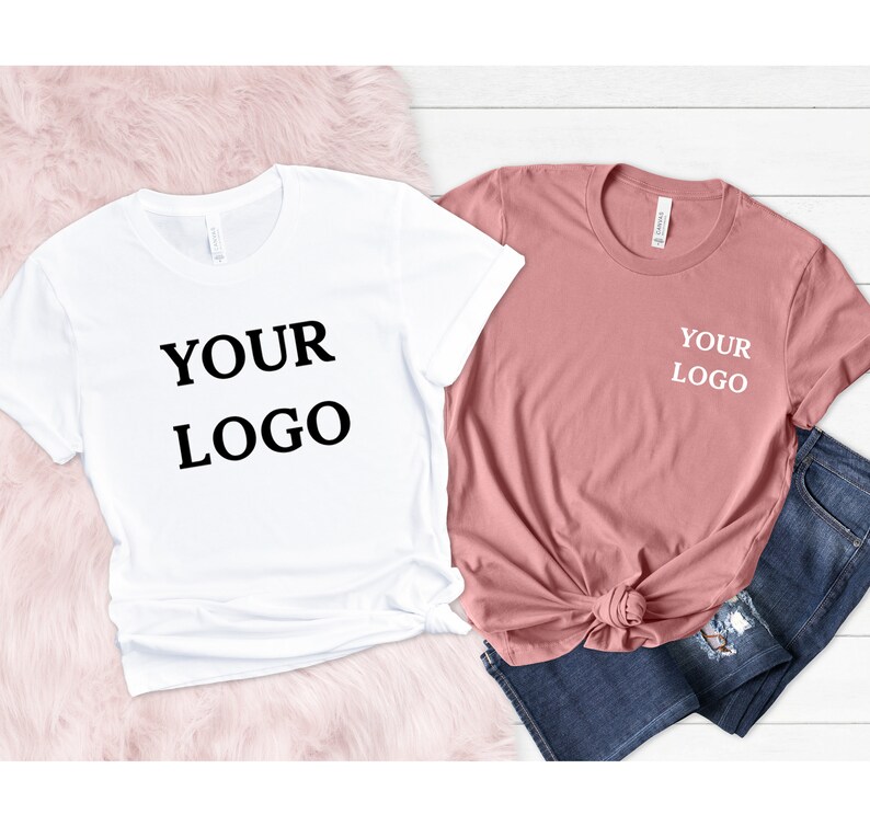 Puede incluir: Dos camisetas, una blanca y otra rosa, ambas con el texto "YOUR LOGO" impreso en ellas. La camiseta blanca tiene el texto impreso en negro, mientras que la camiseta rosa tiene el texto impreso en blanco.