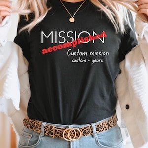 Peut inclure: Un t-shirt noir avec le texte "MISSION accomplie" en blanc, le mot "accomplie" barré en rouge. Le texte "Mission personnalisée personnalisée - années" est imprimé en blanc en dessous.