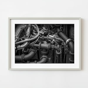 May include: A black and white framed photograph depicting a complex network of industrial metal pipes and joints. The composition features various curved and straight cylindrical segments connected by bolted flanges, creating a dense, intricate web.
