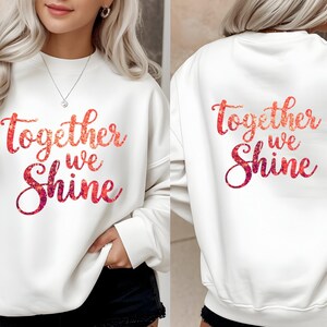 May include: White sweatshirt with the text "Together we Shine" in a red and pink floral design on the front and back. The sweatshirt has long sleeves and a crew neck.