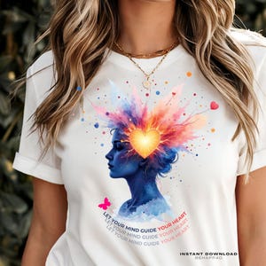 Peut inclure: T-shirt blanc avec une illustration vibrante d'une silhouette bleue avec un cœur au centre, entourée d'éclats colorés. Le texte "LET YOUR MIND GUIDE YOUR HEART" est imprimé sur le t-shirt, ainsi que "INSTANT DOWNLOAD BEHAPP40".