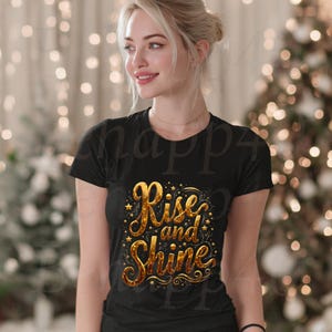 Könnte beinhalten: Schwarzes T-Shirt mit dem goldenen Schriftzug „Rise and Shine“ und Sternen. Das Shirt hat kurze Ärmel und einen Rundhalsausschnitt. Das Design befindet sich mittig auf der Vorderseite.