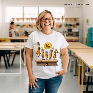 May include: White t-shirt featuring a cartoon illustration of pencils on a wooden platform. The pencils have surprised expressions, with one saying "Who's Next?!" in a yellow speech bubble. The shirt also has the text "BEHAPP40".