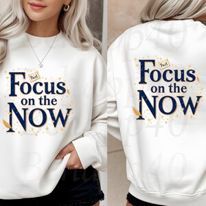 Peut inclure: Sweat-shirt blanc avec l'inscription "Focus on the Now" en bleu marine, avec des accents dorés et un motif de plume. Le sweat-shirt est présenté de face et de dos.
