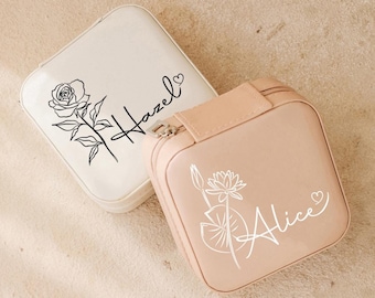 May include: Two small square jewelry boxes with zipper closures. The box on the left is white with a black line drawing of a rose and the name "Hazel" with a heart. The box on the right is light pink with a white line drawing of a water lily and the name "Alice" with a heart.