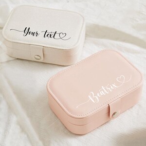 May include: Two rectangular jewelry boxes. One is off-white with the text "Your text" in cursive. The other is pink with the name "Beatrix" in cursive. Both have a heart symbol and a snap closure.