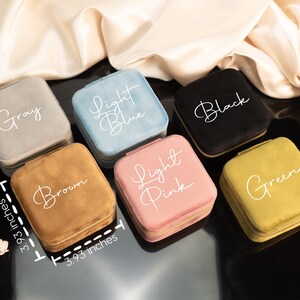 May include: Six velvet jewelry boxes in different colors, each with a different color name written on the top. The colors are gray, light blue, black, brown, light pink, and green. Each box measures 3.93 inches by 3.93 inches.