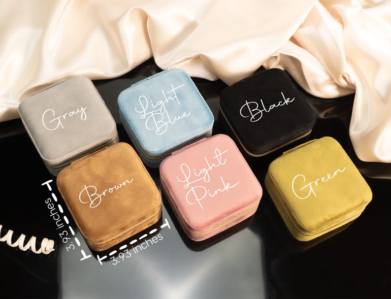 May include: Six velvet jewelry boxes in different colors, each with a different color name written on the top. The colors are gray, light blue, black, brown, light pink, and green. Each box measures 3.93 inches by 3.93 inches.
