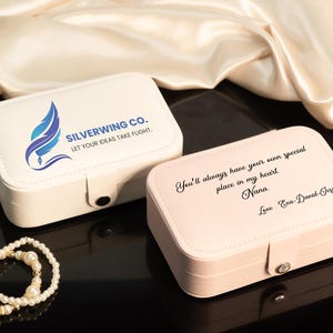 May include: Two rectangular jewelry boxes, one white and one pink, with a pearl bracelet. The white box has the text "SILVERWING CO. LET YOUR IDEAS TAKE FLIGHT." The pink box has a handwritten message.