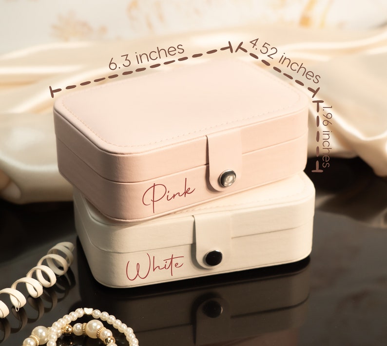 May include: Two jewelry boxes, one pink and one white, stacked on top of each other. The pink box is 6.3 inches long, 4.52 inches wide, and 1.96 inches tall. The pink box has the word "Pink" written on it. The white box has the word "White" written on it.