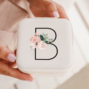 May include: White jewelry box with a zipper closure. The box has a floral design with a pink and white flower and green leaves. The letter "B" is in black outlined in white.