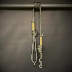 May include: An olive green and tan dog lead and matching collar. The lead is made of a thick, braided rope with a metal clasp and a loop. The collar has a metal ring. The lead is knotted.