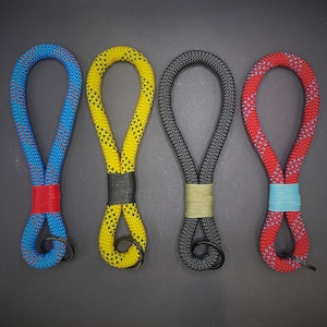 May include: Four rope keyrings in blue, yellow, grey, and red. Each keyring has a contrasting band and a black metal ring. The blue and red keyrings have a pattern of red and blue. The yellow keyring has a black band.