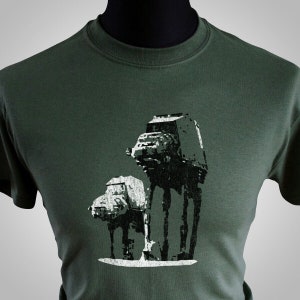以下が含まれることがあります： スターウォーズのAT-ATウォーカー2体の白いシルエットが描かれた緑色のTシャツです。