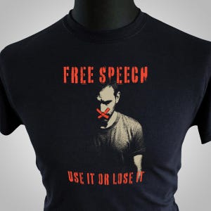 May include: Black t-shirt featuring the words "FREE SPEECH" and "USE IT OR LOSE IT" in a distressed red font. A graphic of a man with a red "X" over his mouth is below the text. The shirt is displayed on a black mannequin.