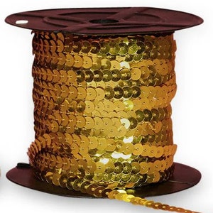May include: A spool of gold sequin trim. The trim is made of small, round, shiny sequins sewn together in a continuous line. The spool is dark brown and the sequins are a bright, metallic gold color. The trim is likely used for embellishing clothing or crafts.