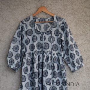 Könnte beinhalten: Ein hellblaues Baumwollkleid mit einem runden, blau-weißen Druck. Das Kleid hat einen V-Ausschnitt und 3/4-Ärmel. Das Kleid ist in der Taille gerafft und hat einen Bindegürtel vorne. Das Kleid ist mit "BlessIndia" gekennzeichnet.