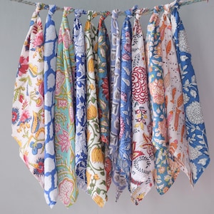 May include: Ten patterned fabric squares in various colours, including blue, pink, and yellow, hang from a rope. The fabrics display floral and geometric designs. The textiles are knotted at the top, creating a colourful and decorative display.