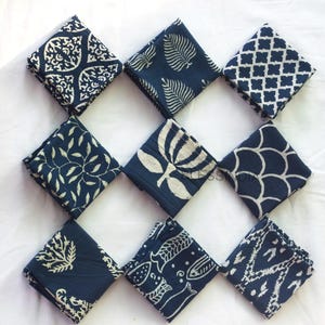 May include: A set of nine square fabric napkins arranged in a grid, each featuring a distinct dark navy blue and white block-printed pattern, including floral, leaf, geometric, fish, and scale motifs, showcasing a variety of textile designs.