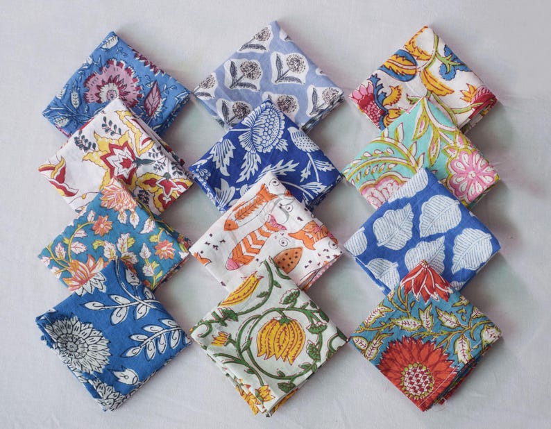 May include: A set of 12 colorful cotton napkins with floral and geometric patterns. The napkins are folded and arranged in a square shape. The napkins are a mix of blue, white, orange, red, and green.