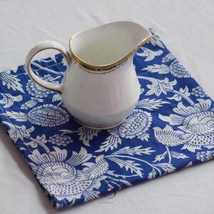May include: A white ceramic creamer with a gold trim sits on a blue and white floral patterned fabric napkin.