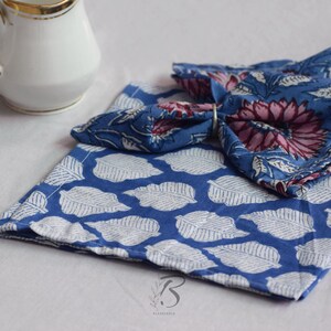 May include: Two blue and white cotton napkins with a floral print. The top napkin is folded into a triangle shape and has a pink and blue floral design. The bottom napkin has a white leaf pattern on a blue background.