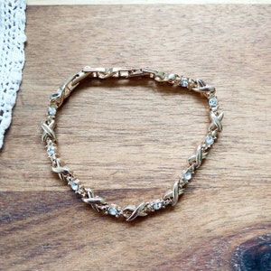 May include: A gold-tone bracelet with a delicate, interwoven chain design. The bracelet is adorned with small, clear rhinestones.
