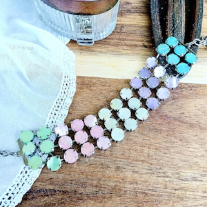 May include: A multi-colored iridescent bracelet with a gradient of turquoise, purple, pink, and green. The bracelet is made of small round beads connected by silver metal links.