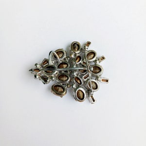 May include: A silver tone brooch with a cluster of brown rhinestones in the shape of a tree. The brooch has a pin back.
